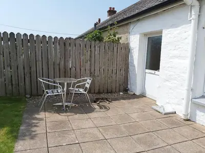 a patio with a table and two chairs and a dog at Poppy's Place Annex in Camelford North Cornwall in Camelford