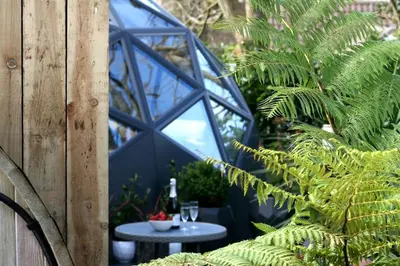 a glass greenhouse with a table and a glass window at Romance - Stargazing - Hot tub & sauna! in Camborne