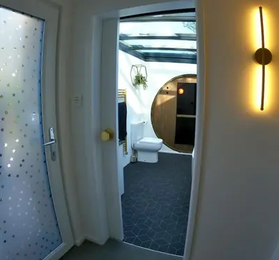 a bathroom with a toilet and a door with a mirror at Romance - Stargazing - Hot tub & sauna! in Camborne