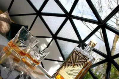 a bottle of alcohol sitting on a table with glasses at Romance - Stargazing - Hot tub & sauna! in Camborne