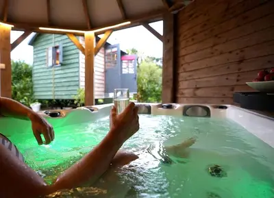 a person holding a glass of water in a hot tub at Romantic Retreat - Luxury Shepherds Hut + Hot Tub! in Camborne