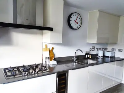 a kitchen with white cabinets and a clock on the wall at Tolcarne - Perranporth Cornwall in Perranporth