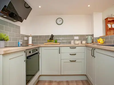 a kitchen with white cabinets and a clock on the wall at Trelawney Cottage in Charlestown