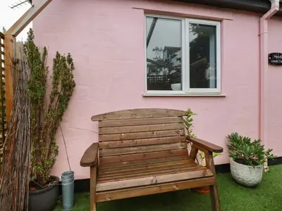 a wooden bench sitting in front of a pink house at Melvill Lower Deck in Falmouth