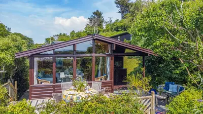 a glass house with a table in a garden at Scandinavian Style Lodge in Rock in Wadebridge