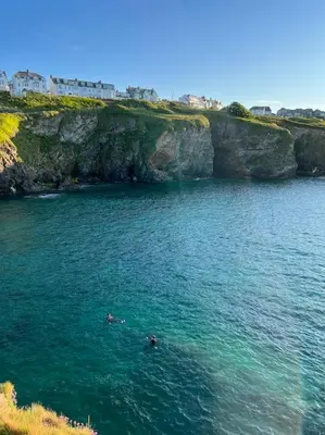 two people swimming in the water next to a cliff at Wheelwright House in Bodmin