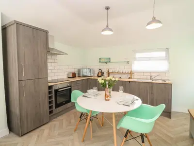 a kitchen with a white table and green chairs at Byghan Thornton in Redruth