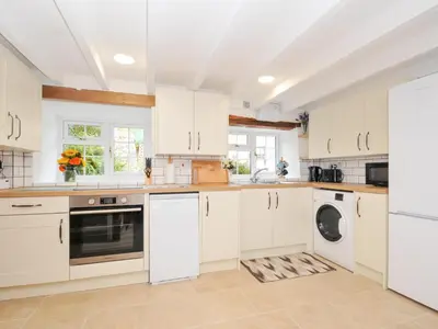 a kitchen with white cabinets and a washer and dryer at Henwood Barn in Liskeard