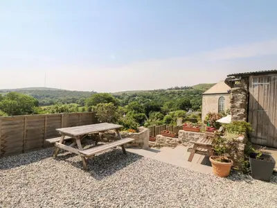a patio with a wooden picnic table and a view at Henwood Barn in Liskeard