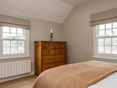 a bedroom with a wooden dresser and two windows at Mermaid Cottage in Port Isaac