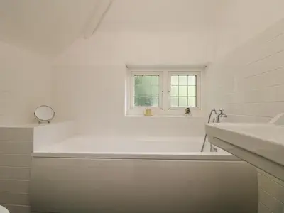 a white bathroom with a tub and a window at Flushing Meadow in Helston
