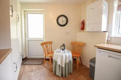 a kitchen with a table and chairs and a clock on the wall at Sunny Corner Cottage in Hayle