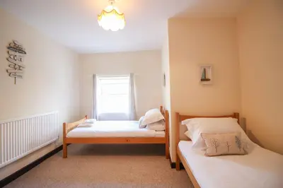 a bedroom with two beds and a window at Sunny Corner Cottage in Hayle