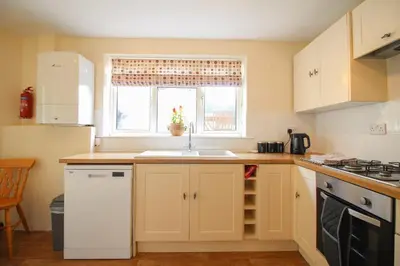 a kitchen with white cabinets and a sink and a window at Sunny Corner Cottage in Hayle