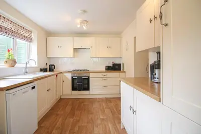 a kitchen with white cabinets and a wooden floor at Sunny Corner Cottage in Hayle