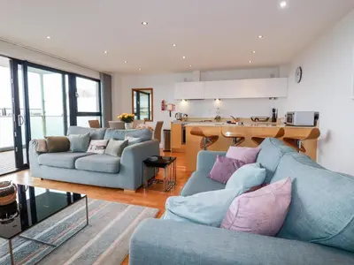 a living room with two blue couches and a kitchen at Fistral Pearl in Newquay