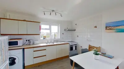 a kitchen with white cabinets and a table and a microwave at F11 Roslyn, Riviere Towans in Hayle