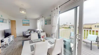 a living room with a table and chairs and a balcony at F24 Glenara, Riviere Towans in Hayle