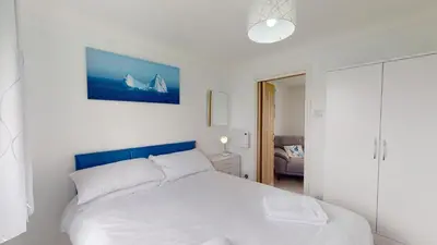 a bedroom with a white bed with a blue headboard at F24 Glenara, Riviere Towans in Hayle