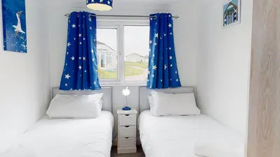 two twin beds in a room with blue curtains at F24 Glenara, Riviere Towans in Hayle
