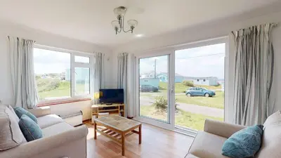 a living room with a couch and a tv and windows at F30 Fernside, Riviere Towans in Hayle