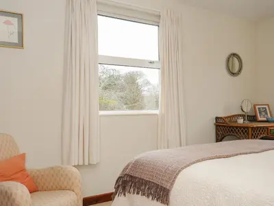 a bedroom with a bed and a window and a chair at Kirland in Wadebridge