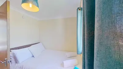 a bedroom with a white bed and a blue curtain at F49 Junesta, Riviere Towans in Hayle