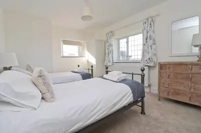 a bedroom with two beds and a dresser and two windows at WALK TO THE BEACH, spacious cottage with sea views in St Merryn
