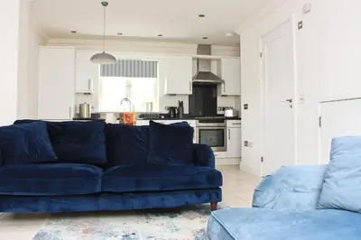 a living room with a blue couch and a kitchen at BEACHSIDE modern home, dogs welcome in St Merryn