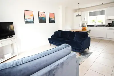 a living room with two blue couches and a kitchen at BEACHSIDE modern home, dogs welcome in St Merryn