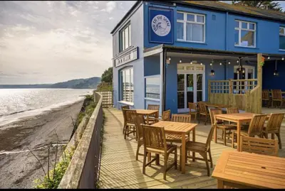a blue building with tables and chairs next to the water at Torpoint - Apartment - Sleeps4 - Seaside - Parking in Torpoint