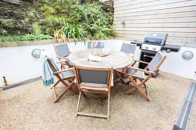 a wooden table with four chairs and a stove at Beach Lovers Paradise in Portreath - With Sea Views & Log Burner just 100m from beach in Portreath