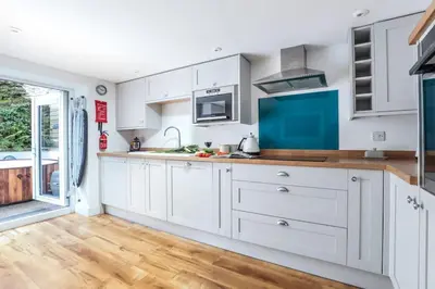 a kitchen with white cabinets and a wooden floor at Beach Lovers Paradise in Portreath - With Sea Views & Log Burner just 100m from beach in Portreath