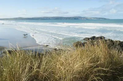 a beach with a person and a surfboard in the water at Towans Retreat, Hayle in Hayle