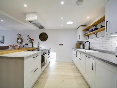 a kitchen with white cabinets and a wooden floor at Joinery Cottage in Porthleven