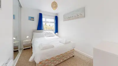 a bedroom with a bed and a window with blue curtains at F15 Brian View, Riviere Towans in Hayle