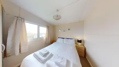 a bedroom with a bed with white sheets and a window at F75 Bronvellan, Riviere Towans in Hayle