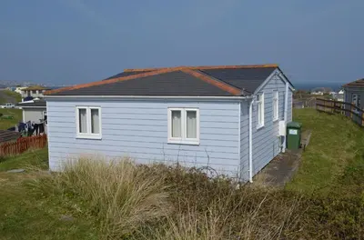 a small white house sitting on top of a field at F18 Branksea, Riviere Towans in Hayle