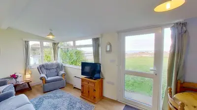 a living room with a tv and a chair and a window at F18 Branksea, Riviere Towans in Hayle