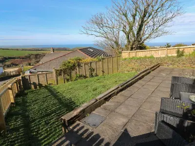 a patio with chairs and a fence and grass at Chilowan in Tintagel