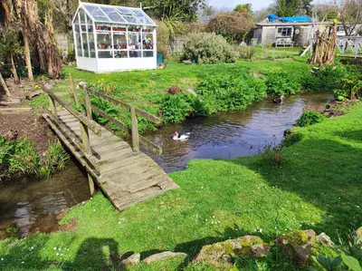 a wooden bridge over a river with a greenhouse at Pleasant streams Barn in St Austell