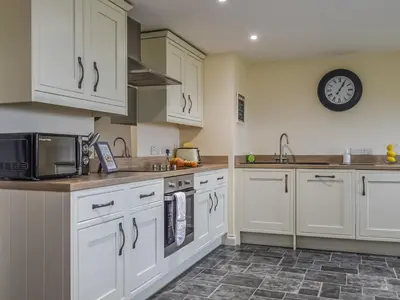 a kitchen with white cabinets and a clock on the wall at Bolivar Barn in Gwennap
