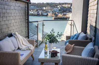 a balcony with chairs and a table with a view of the water at Beach Vista, harbourside in St Ives in St Ives