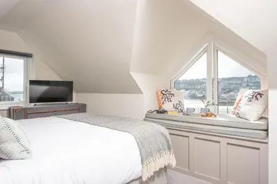 a white bedroom with a bed and a window at Beach Vista, harbourside in St Ives in St Ives