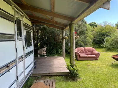a covered porch with a couch and a chair on the grass at The Quarry Caravan in Falmouth