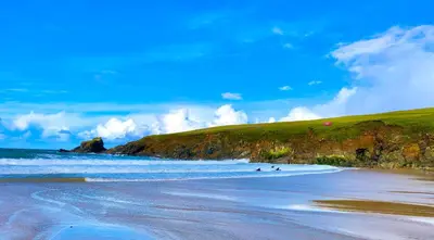 a beach with people in the water and a green hill at Trevone Bay Seaside Home For 4 - Close To Beach and Padstow in Padstow