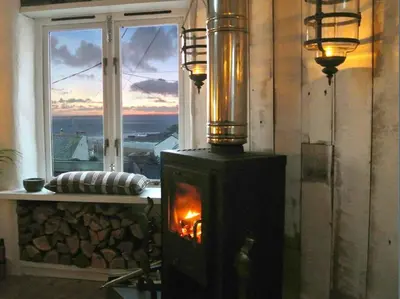 a fireplace in a room with a view of a window at The Old Stores, Luxury beach side selfcatered holiday cottage above the beach in Porthleven