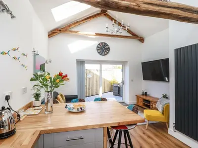 a kitchen and living room with a table and a tv at Harvenna Cottage in Bude
