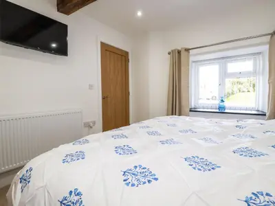 a bedroom with a white and blue bed with a window at Harvenna Cottage in Bude