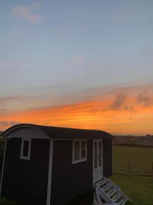 a small house with a sunset in the background at Ewe With A View Sea View Shepherds Huts in Breage